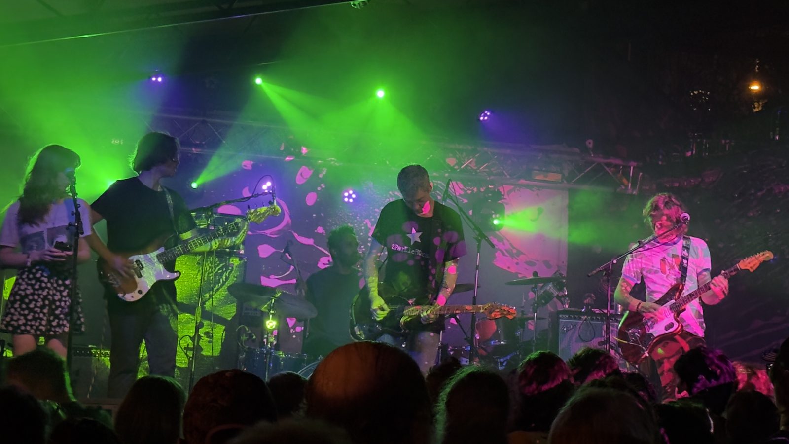 An independent band mid-set under green and magenta stage lights, seen from the crowd